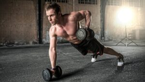 Fitness training. Muscular man holding weights in one armed plank positionpushing up 